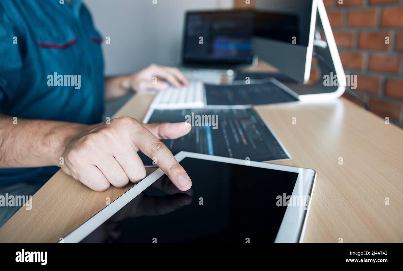 Software developer is pointing to the paper working and analyzing together the code written into the program on the computer. Stock Photo