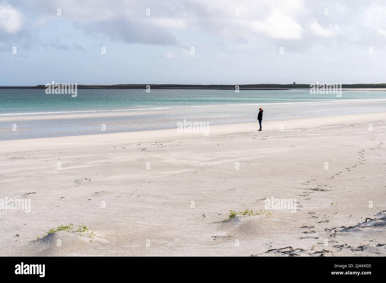 A female tourist stands in the distance looking out to sea on an isolated white sand beach on Sanday, Orkney. Stock Photo