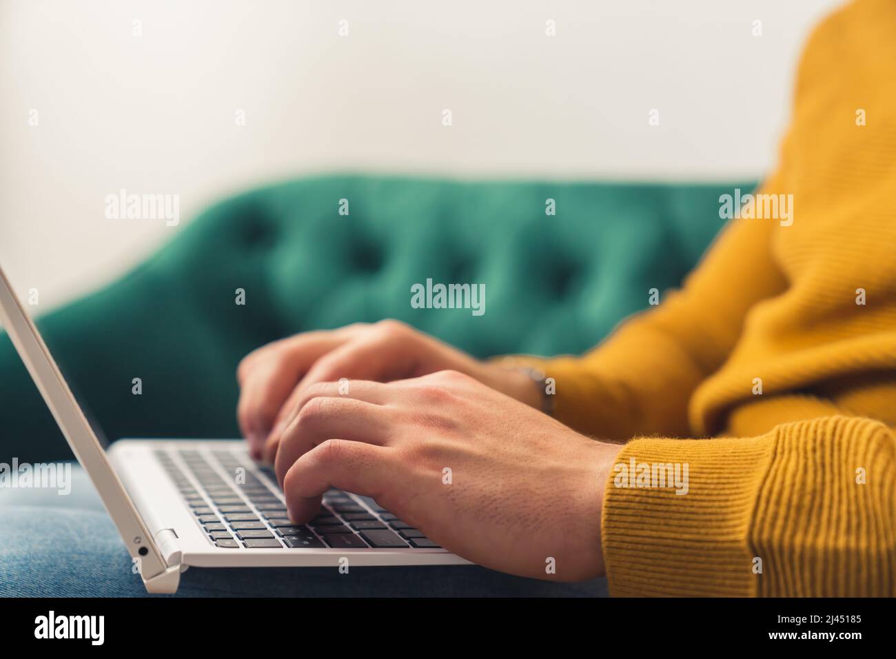 Closeup of Caucasian man working with a laptop on the couch, hands and keyboard visible remote job concept . High quality photo Stock Photo