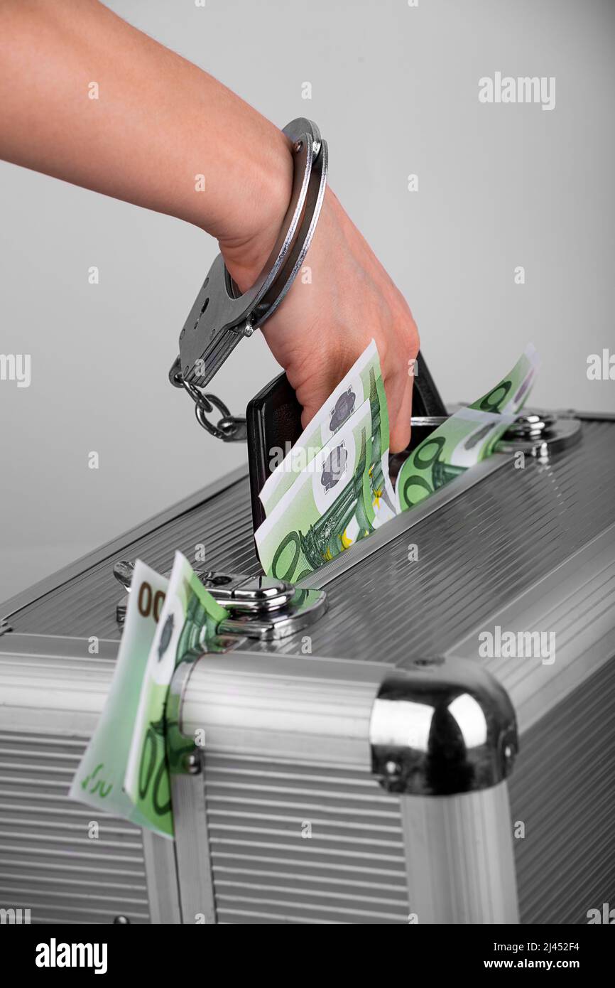 A man's hand handcuffed to a briefcase with money sticking out of it