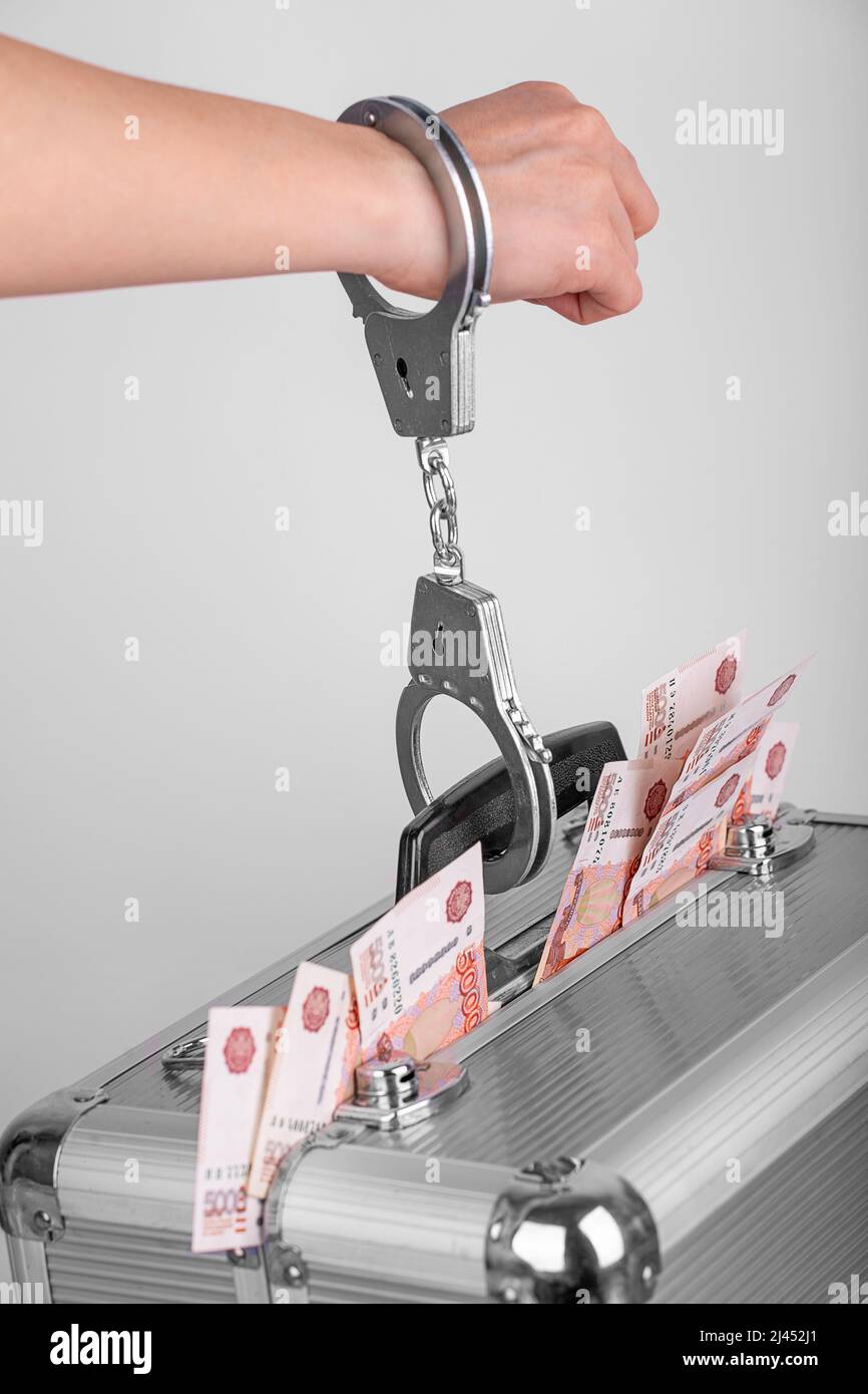 A man's hand handcuffed to a briefcase with money sticking out of it