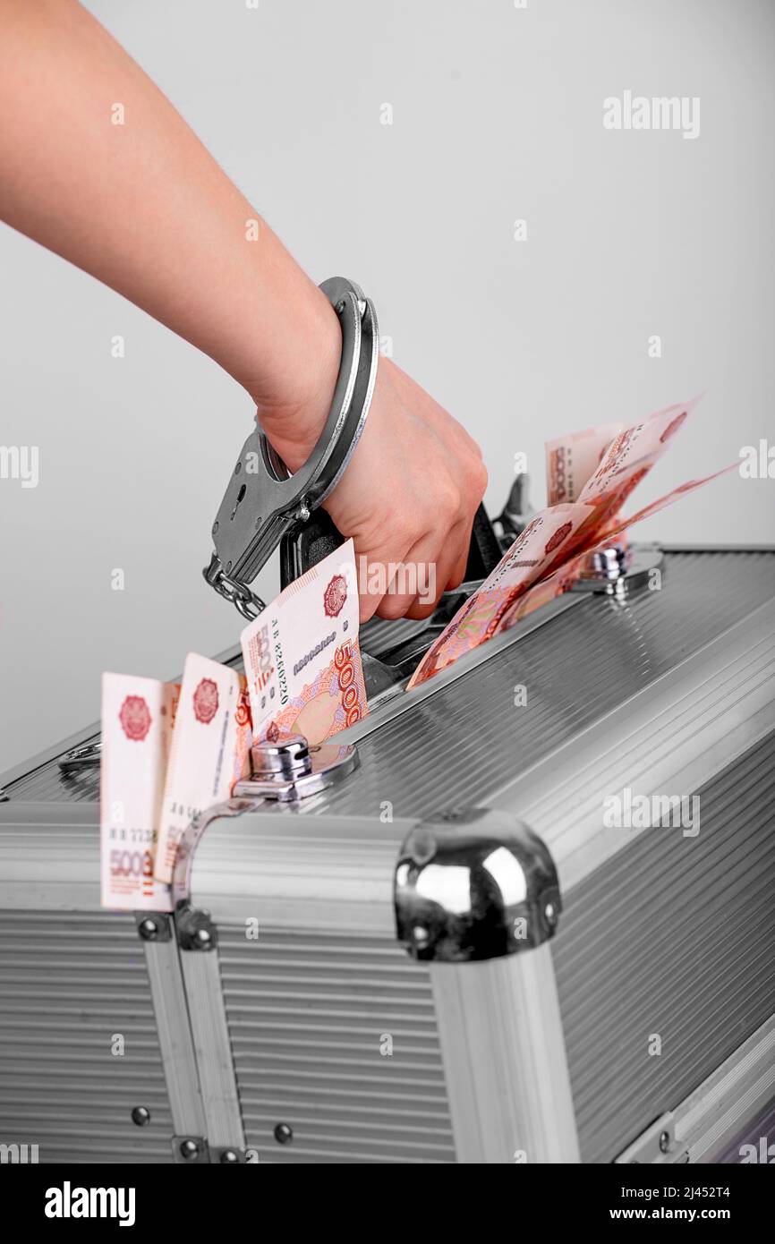 A man's hand handcuffed to a briefcase with money sticking out of it