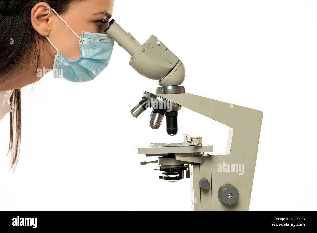 Female scientist with protective face mask looking through a microscope ...