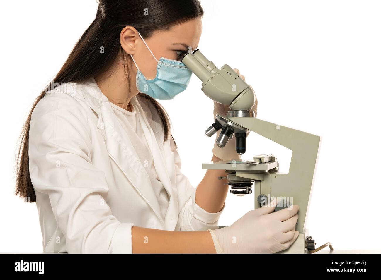 Female scientist with protective face mask looking through a microscope ...