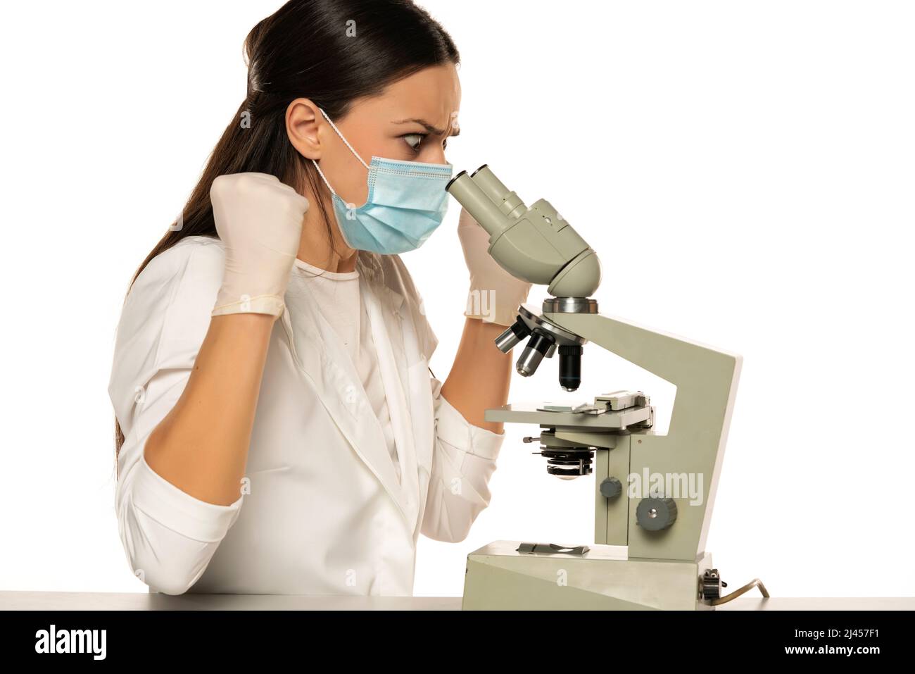 angry-nervous-female-scientist-with-protective-face-mask-looking-through-a-microscope-white-background-2J457F1.jpg