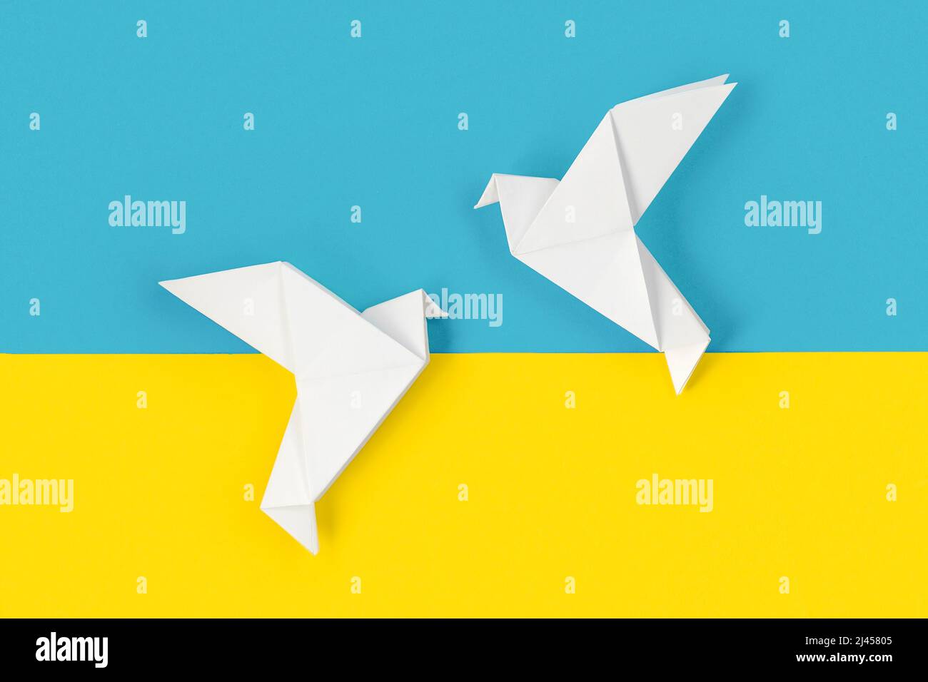 Two white origami paper doves on colors of flag of Ukraine. The concept of peace between two states. Symbol of peace on blue and yellow background. Stock Photo