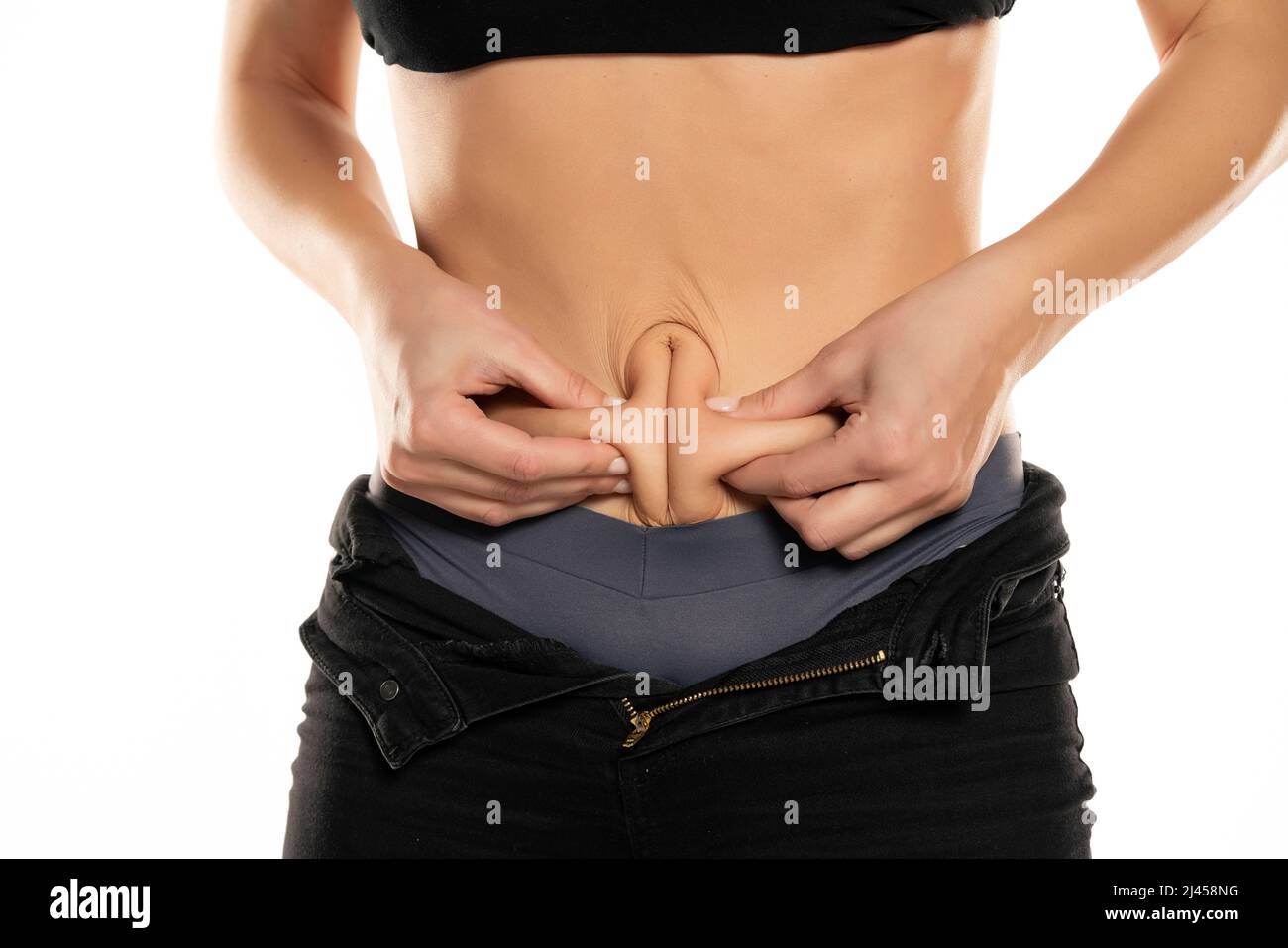 Closeup of a young fit woman pinching her belly on a white background. Stock Photo