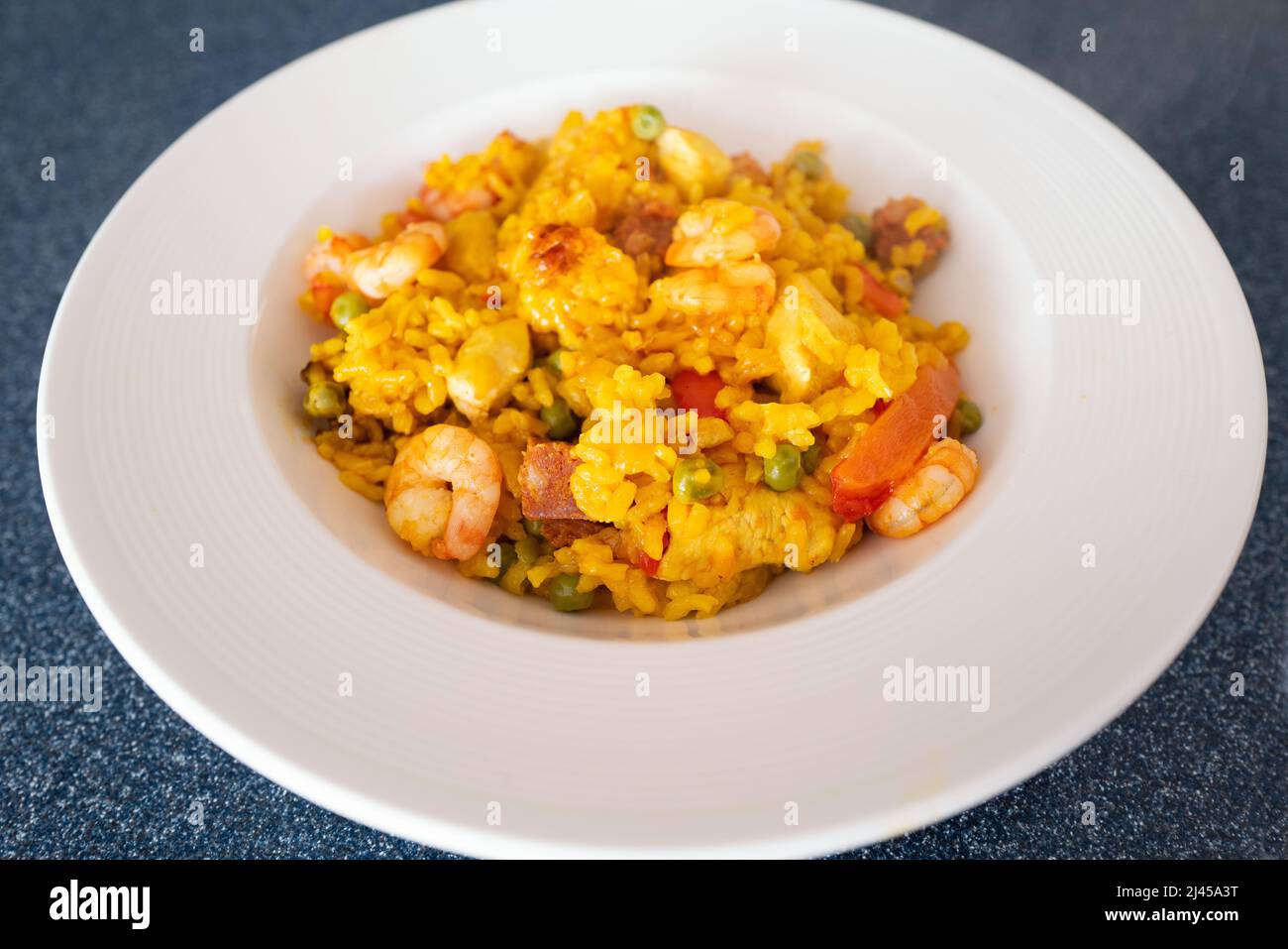 Prawns and chorizo sausage in a home made rice paella dish. There is also chicken with onion, peas and peppers in the meal. It is served in a round wh Stock Photo
