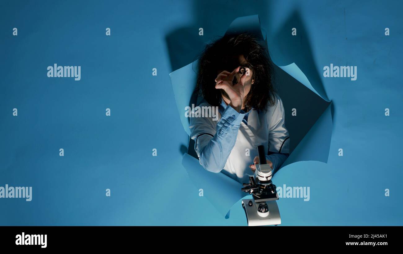 Crazy foolish scientist using laboratory microscope in studio, being