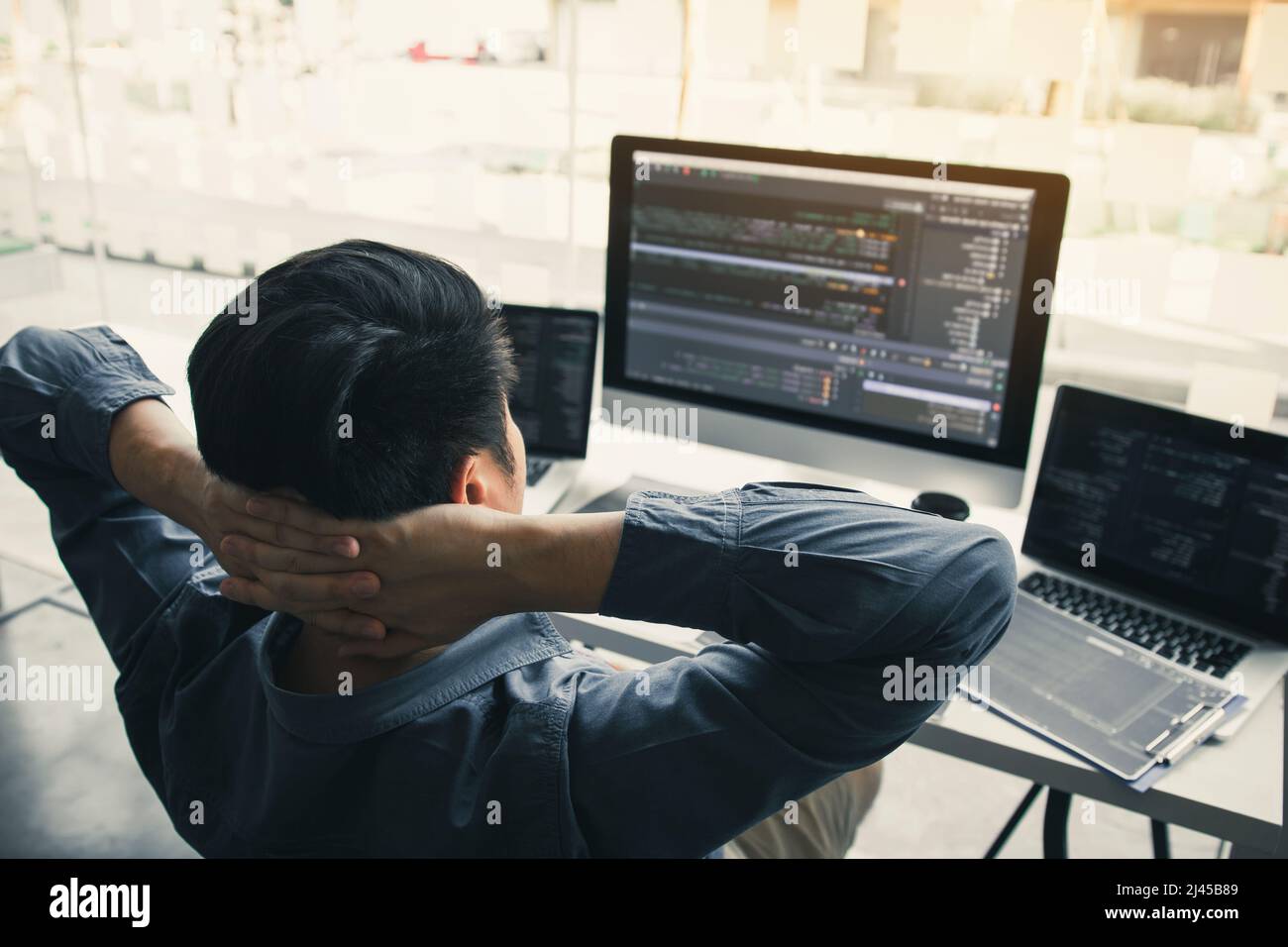 Asian programmers man are relaxing and looking at the code on the computer screen in the office. Stock Photo