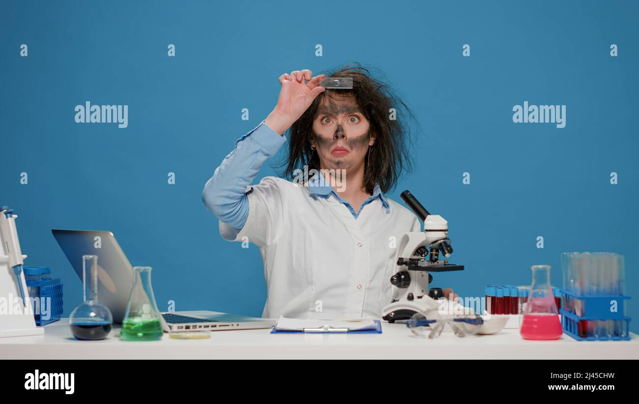 Goofy mad female researcher using microscope at desk, acting crazy and