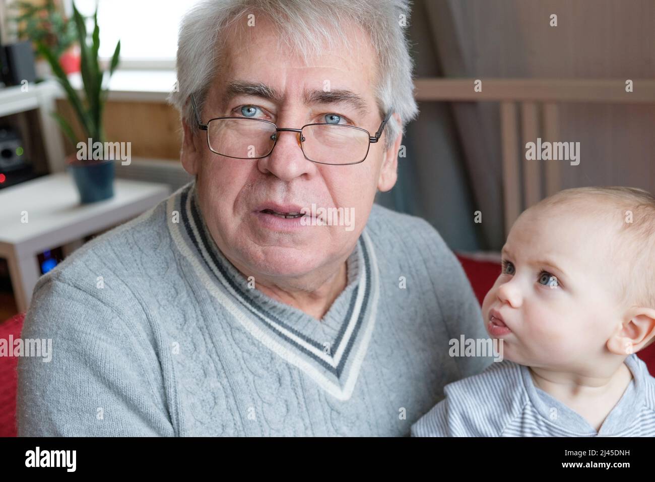 Family Relations of Elderly 60s Male and Baby Girl. Happy Old Man Holds a little Child on Hands. Caucasian Grandchild and Grandfather. Family Time Stock Photo