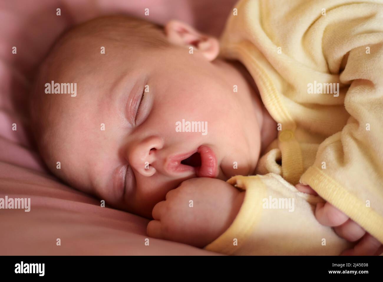 Newborn baby sleep with opened mouth. One, two week age. Infant girl sleeping or waking up while lying on purple bed at home. New life and growing up Stock Photo