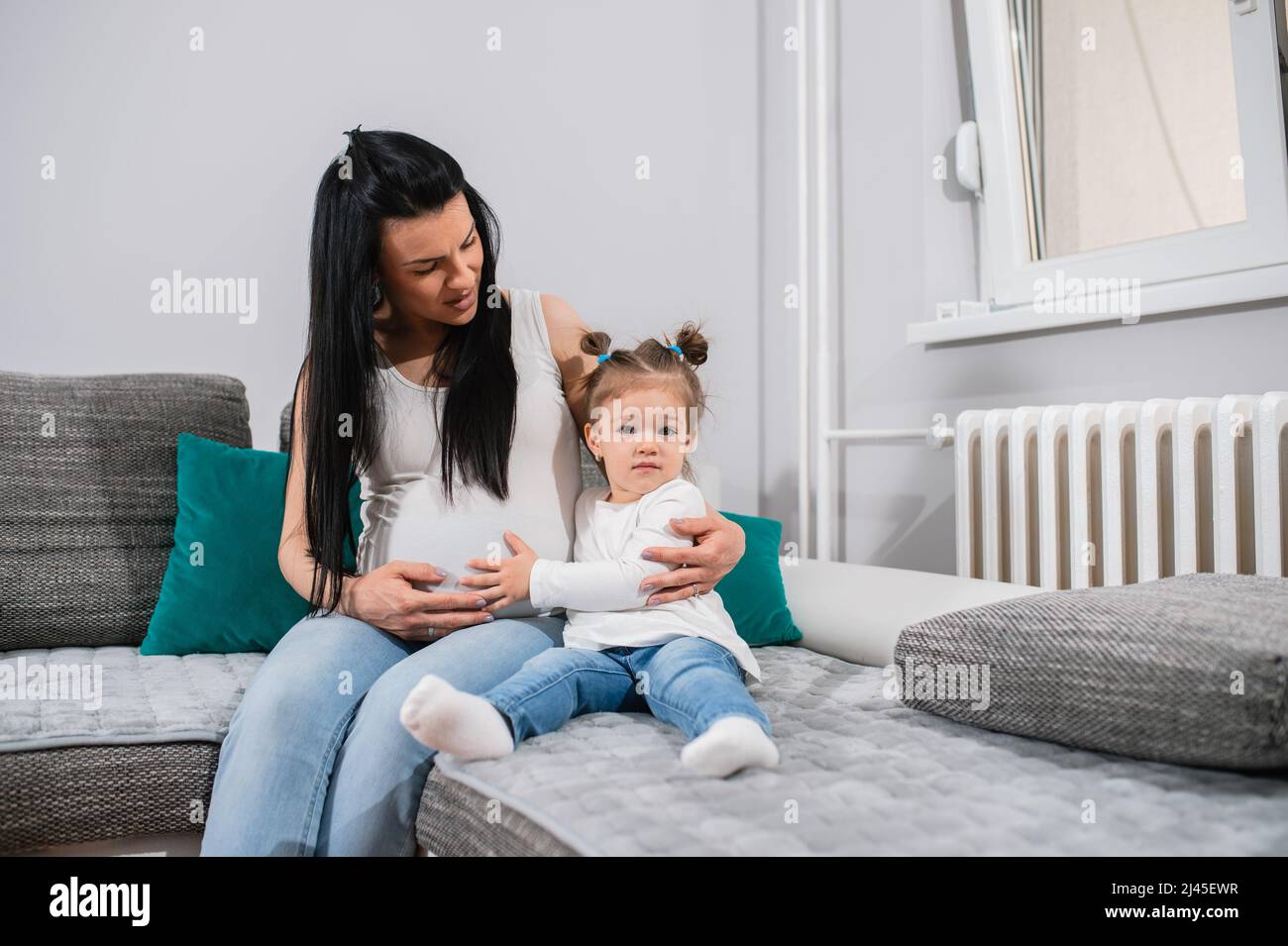 Mother and daughter sit on the couch in the sitting room while little girl cuddles mother's