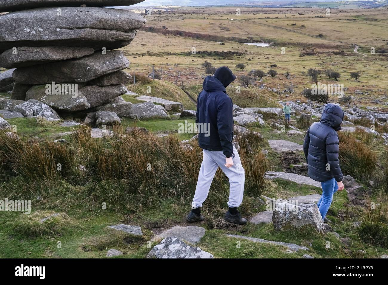 People walking past The Cheesewring a granite rock stack formed by glacial action on Stowes Hill on Bodmin Moor in Cornwall. Stock Photo