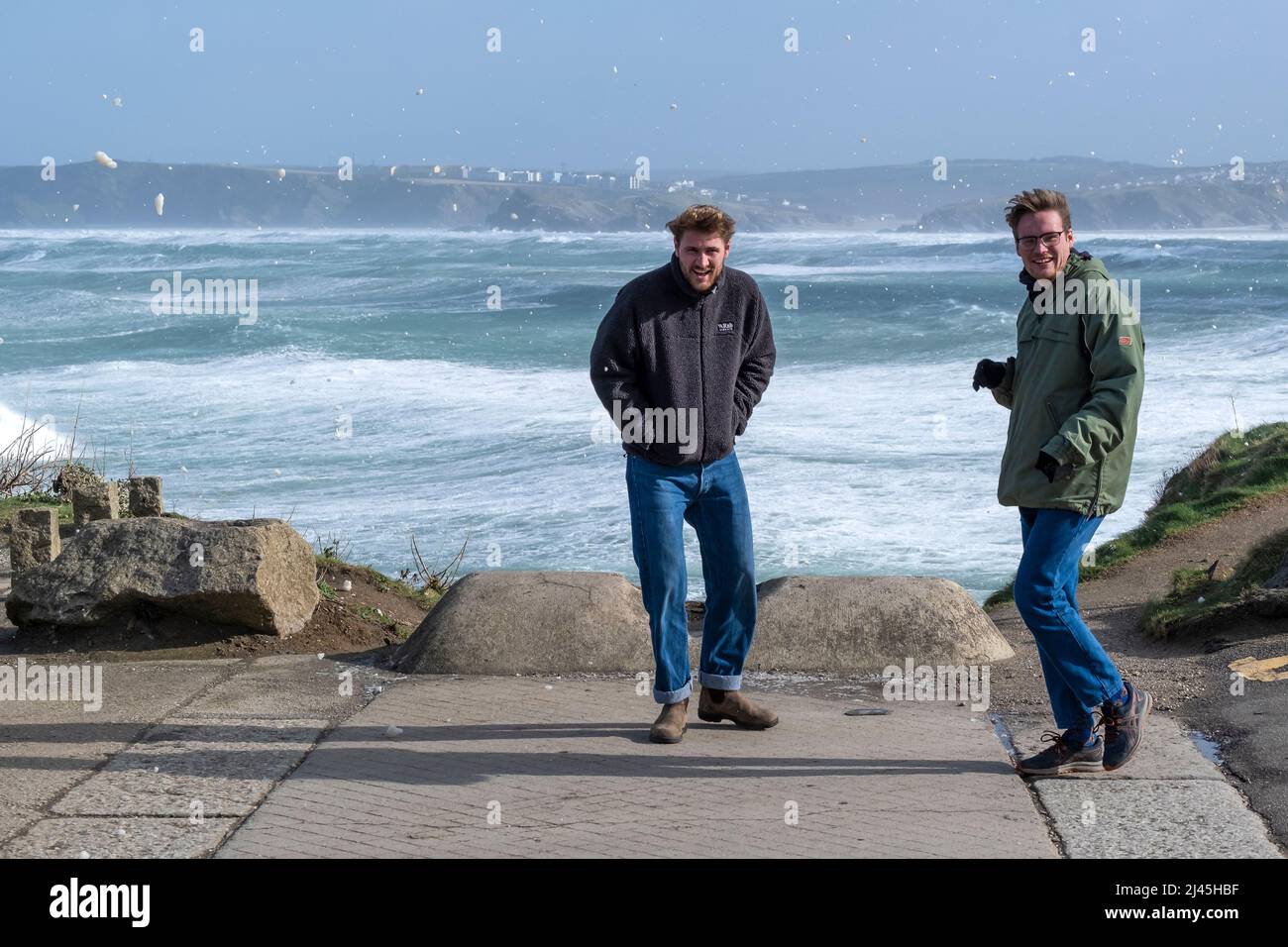 Sea foam blowing around two walkers caused by storm force wind as Storm Eunice reaches Newquay in Cornwall. Stock Photo