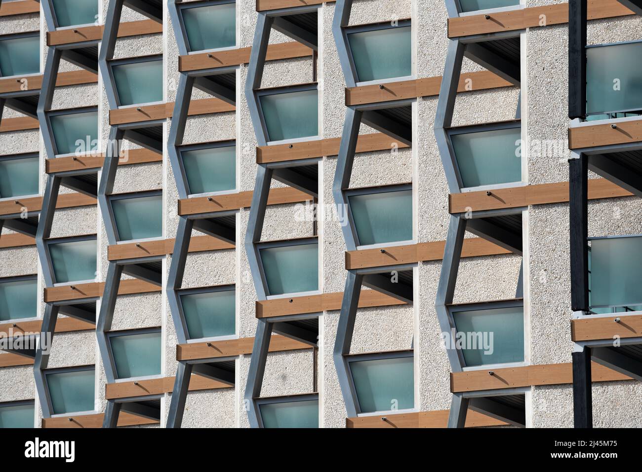 Architectural close-up of building facade of shingle coating with windows and balconies supported by metal beams in symmetric patterns in Chamonix Stock Photo