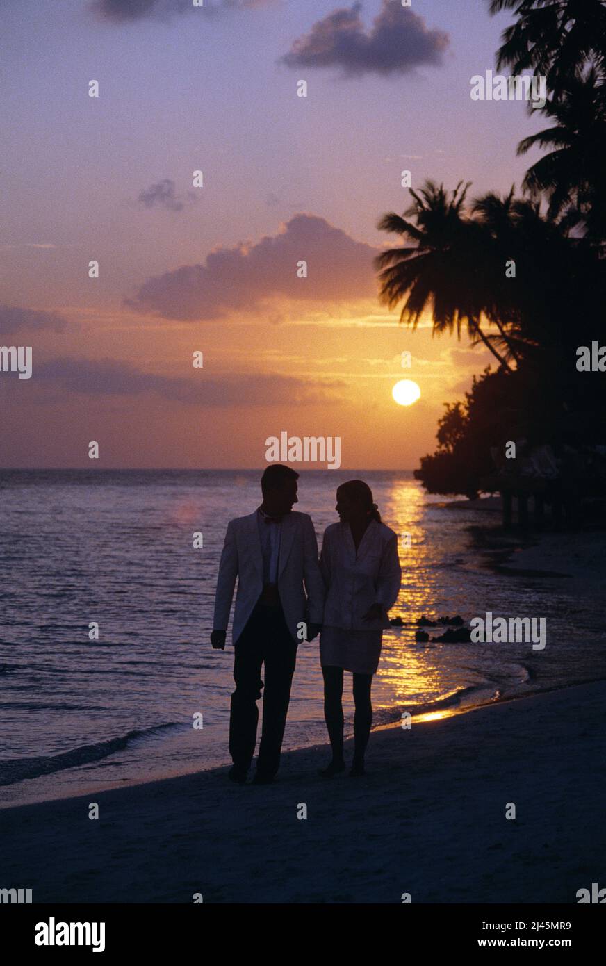 Maldives. Young couple in evening clothes, walking on beach at sunset. Stock Photo