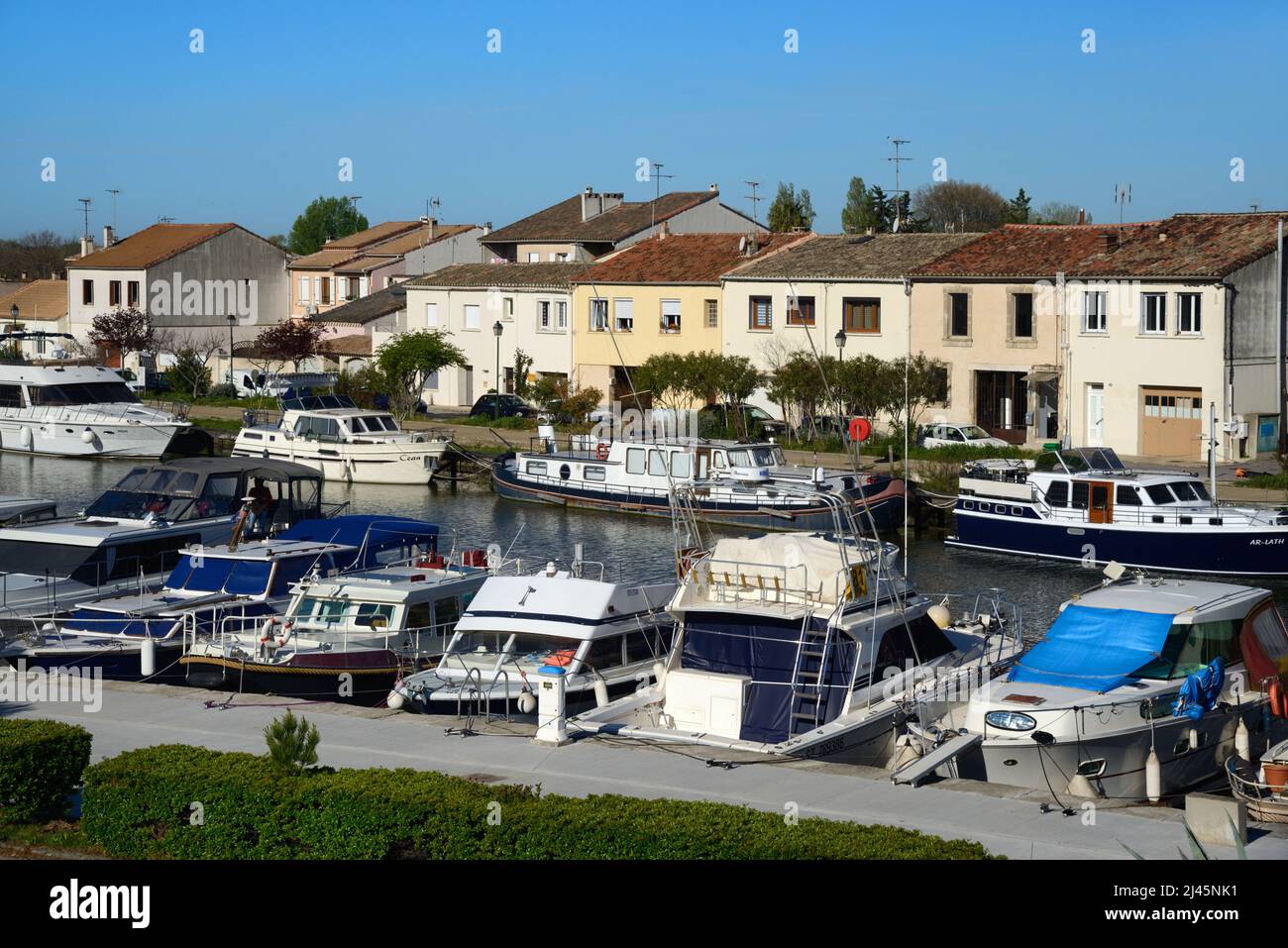 View over Canal Boats and River Boats on the Rhône-Sète Canal and Canalside Houses at Aigues-Mortes Gard France Stock Photo