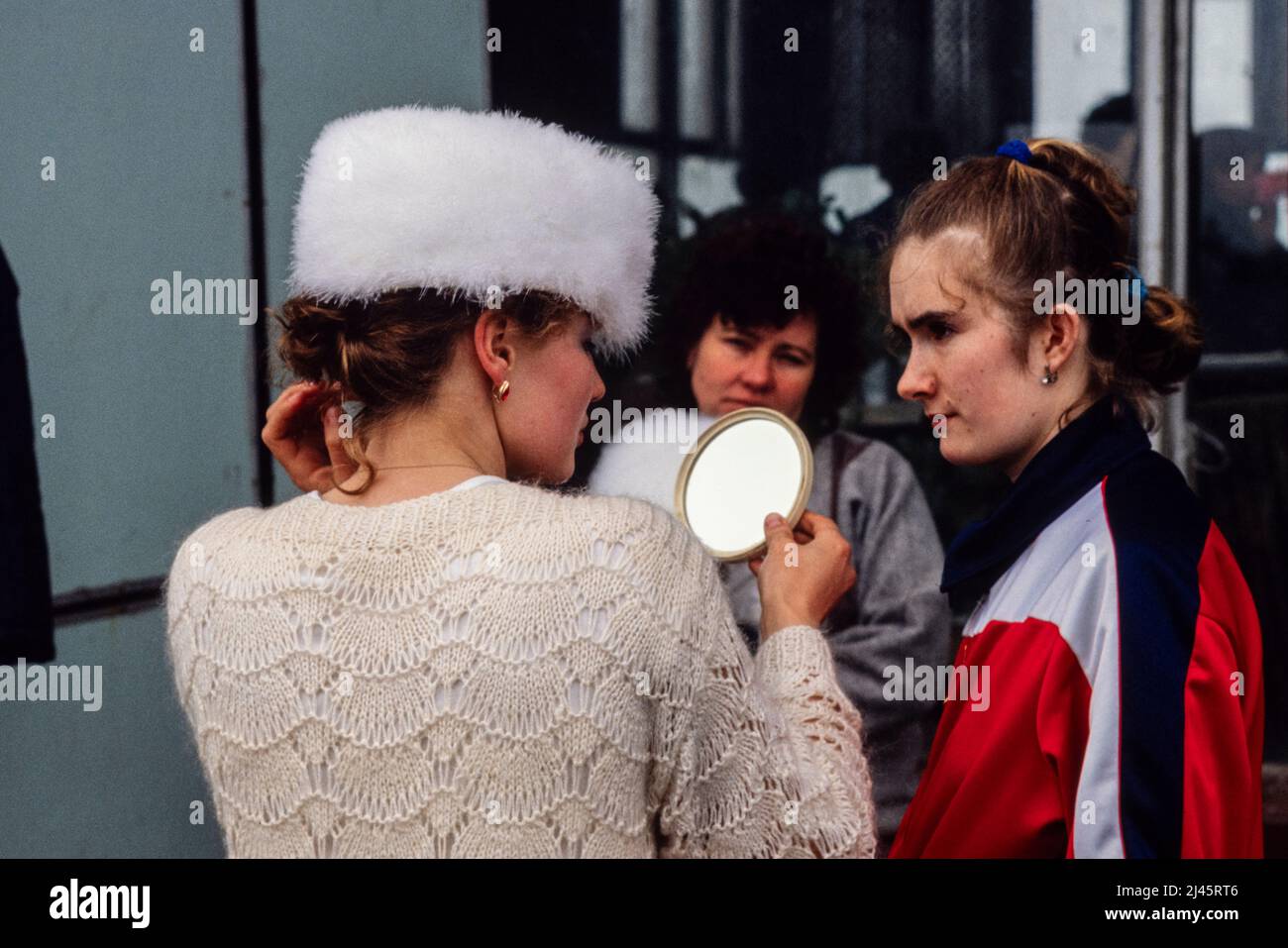 A young woman tries on a white hat with friends at a flea market in Moscow, Russia, May 1990. Stock Photo