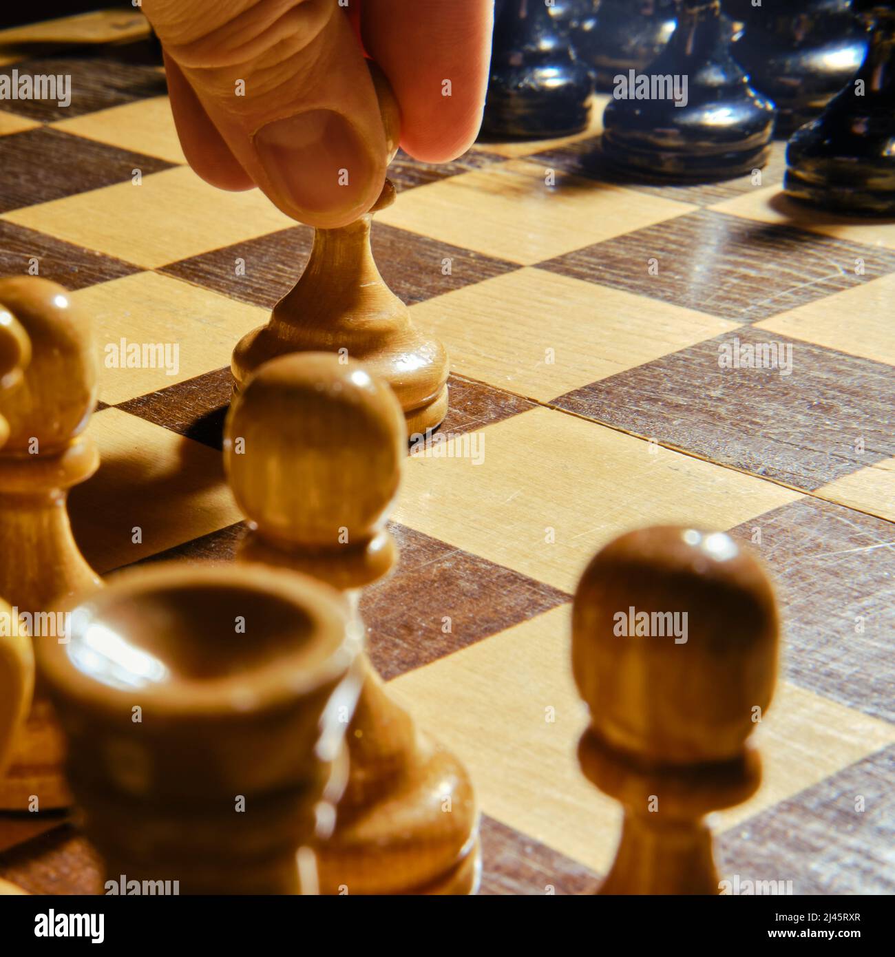 The opening of the chess game with the move of the white king pawn e2-e4,  copy space on a black background. A man hand with a chess piece in a board g