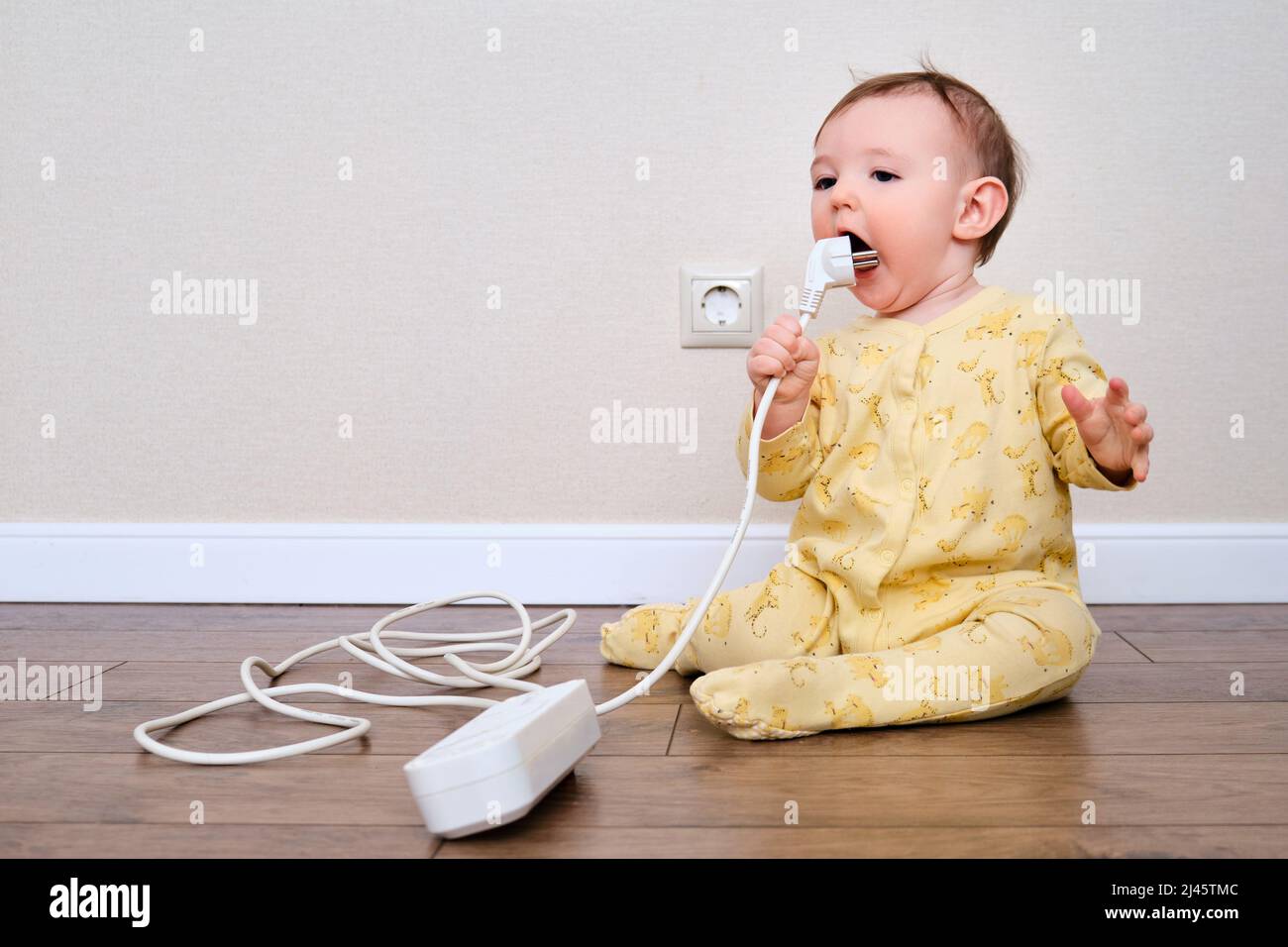 Toddler baby boy gnaws electrical wires while sitting on the floor