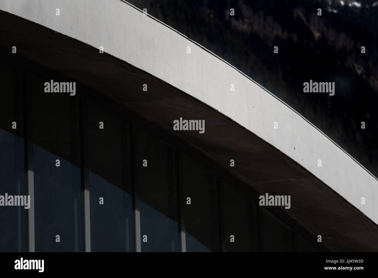 Architecture detail of arched white concrete rooftop beam sloping down over glass and aluminium facade Stock Photo