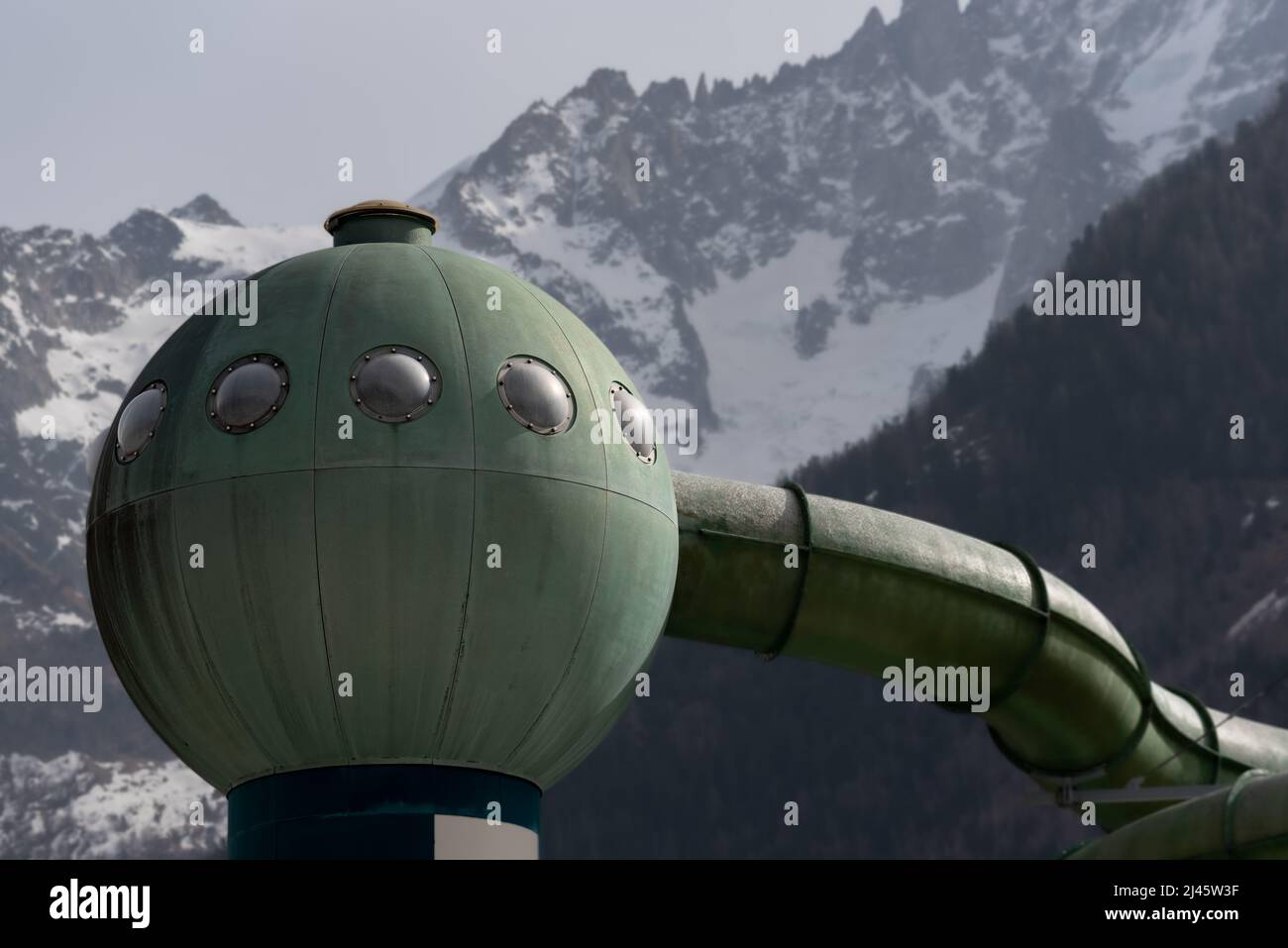 Green sphere and tubes in close-up architectural detail of waterslide feature with background of a mountain ridge in the European Alps Stock Photo