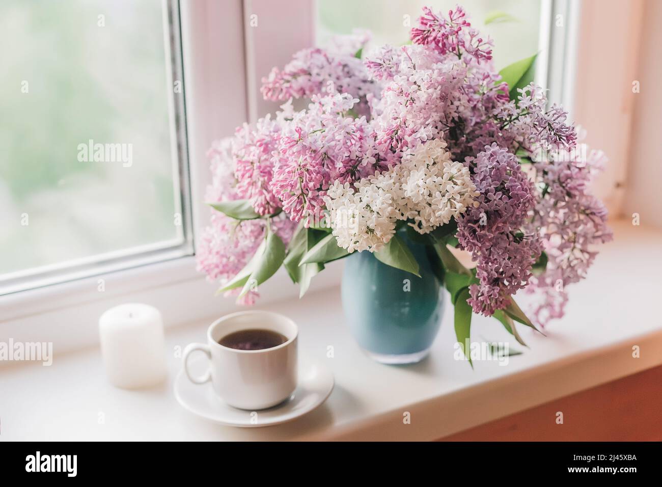 Bouquet of lilacs in a vase,cup of coffee and books on the windowsill. Stock Photo
