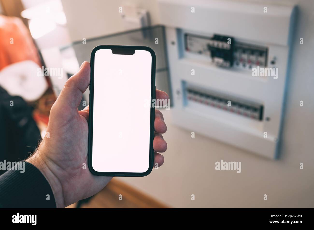 Electrician holding smartphone with blank mockup touch screen in front of circuit breaker box at home, selective focus Stock Photo