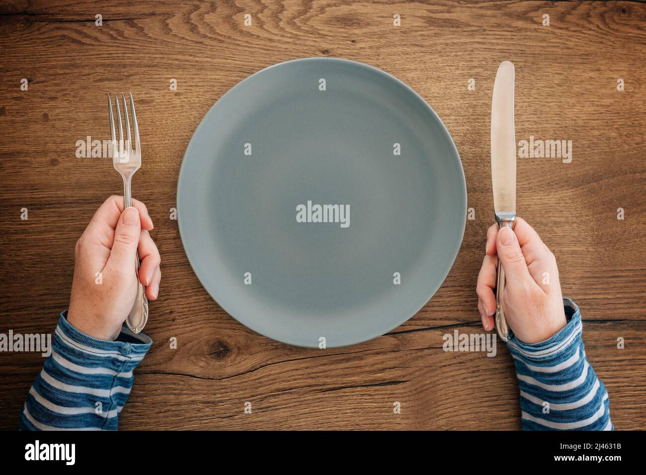 Female hands with fork and knife over empty plate on dining table, top