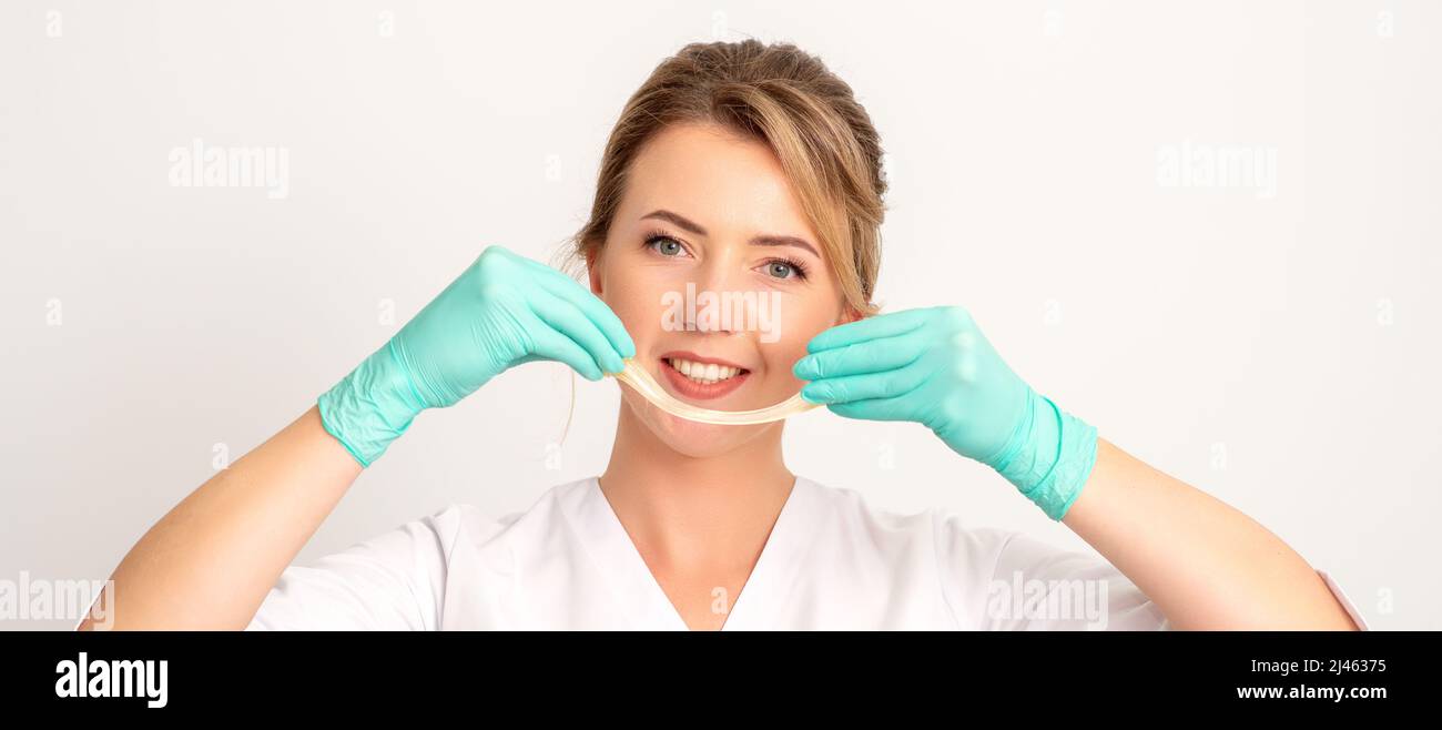 Young caucasian smiling female beautician holding wax for depilation