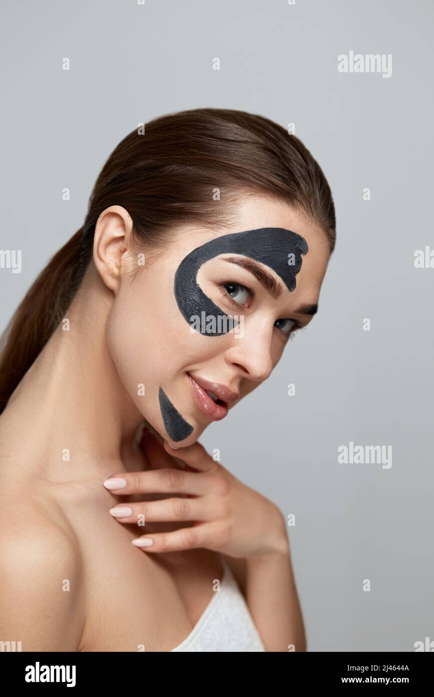 Beauty Facial Mask . Beautiful Young Woman with black mask of clay on face .Skin care .Girl model with cosmetic moisturizer spa mask. Facial treatment Stock Photo