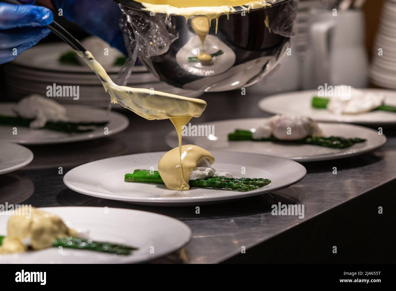 Hollandaise sauce being poured on poached egg and asparagus. Stock Photo