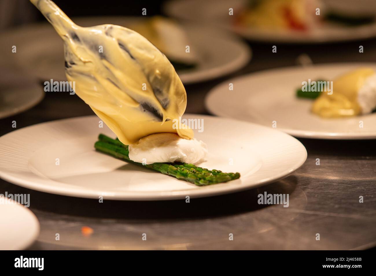 Hollandaise sauce being poured onto poached egg and asparagus. Stock Photo