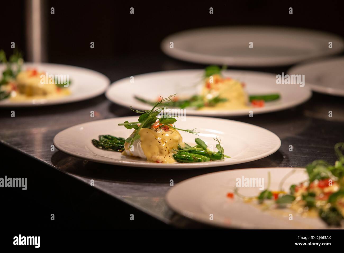 poached egg with asparagus topped with hollandaise sauce during plating up. Stock Photo
