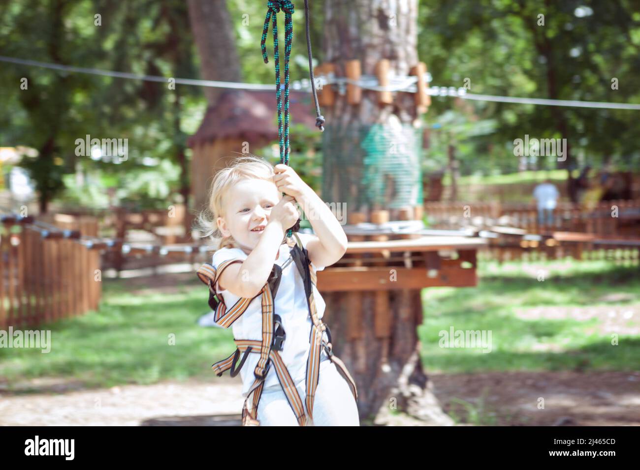 Leisure activity. Little girl on a carbine crosses the rope in an extreme rope park. Stock Photo