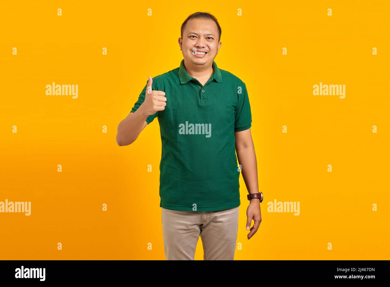 Smiling young Asian man showing approval with thumb up gesture on yellow background Stock Photo