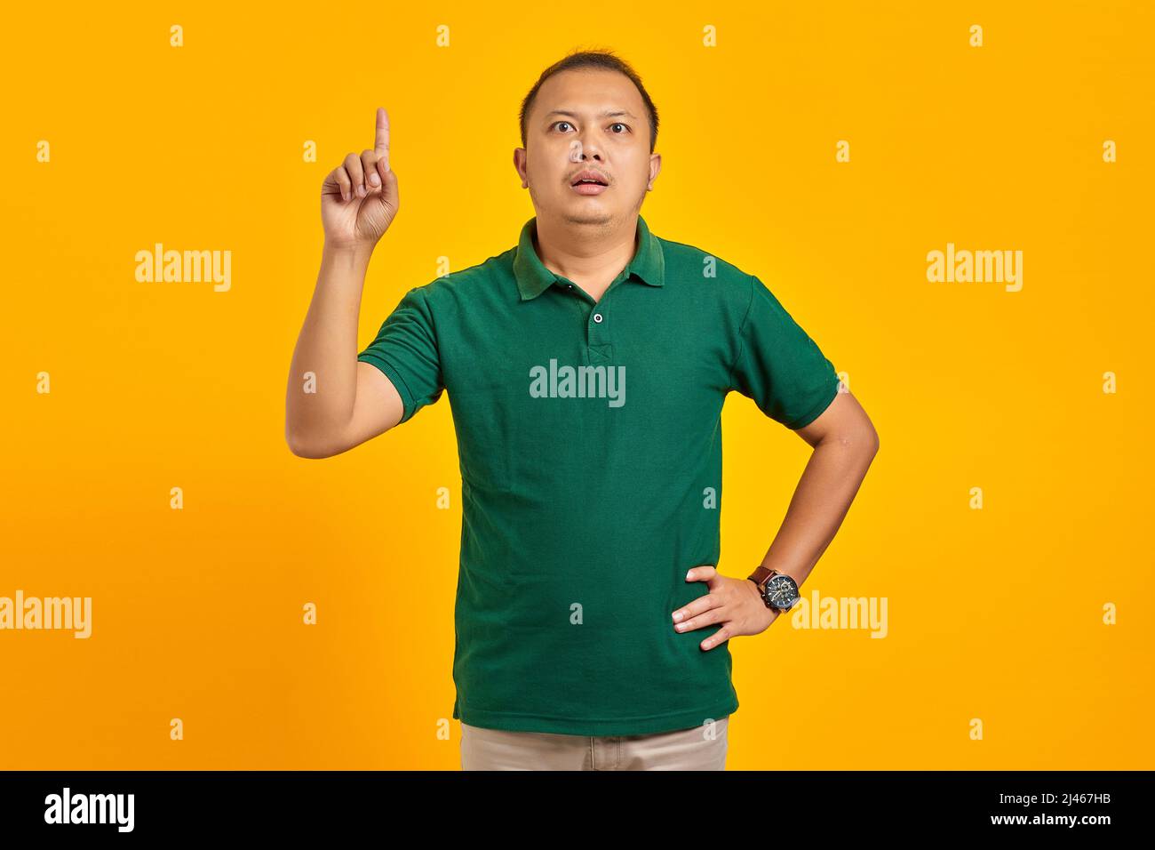 Surprised young Asian man pointing up and having an idea on yellow background Stock Photo