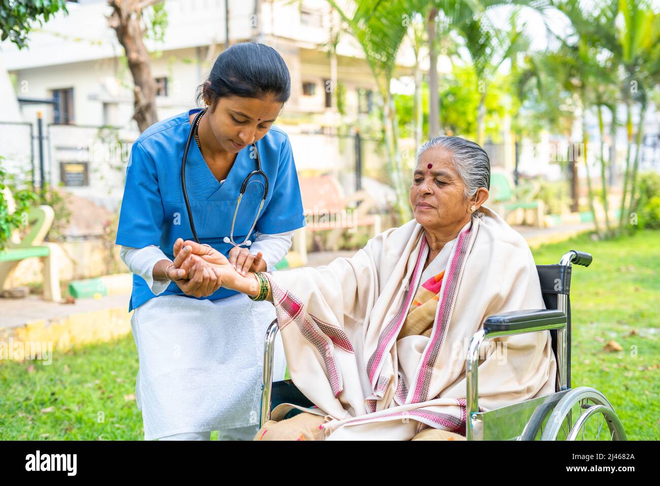 Doctor checking pulse rate of disabled woman while on wheelchair at park - concept of medical care, caretaker and professional occupation Stock Photo