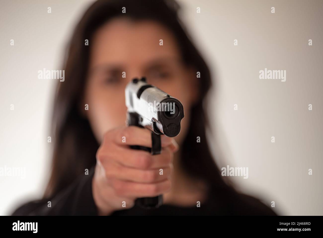 Woman holding a gun in hand pointing at camera. Brunette female secret police agent, killer or spy dark long hair. Selective focus Stock Photo