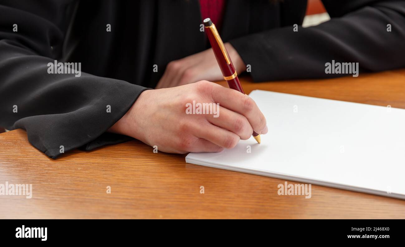 Woman holding a pen on a blank white paper, close up view, wooden office table background. Female hand signing on empty document, copy space Stock Photo