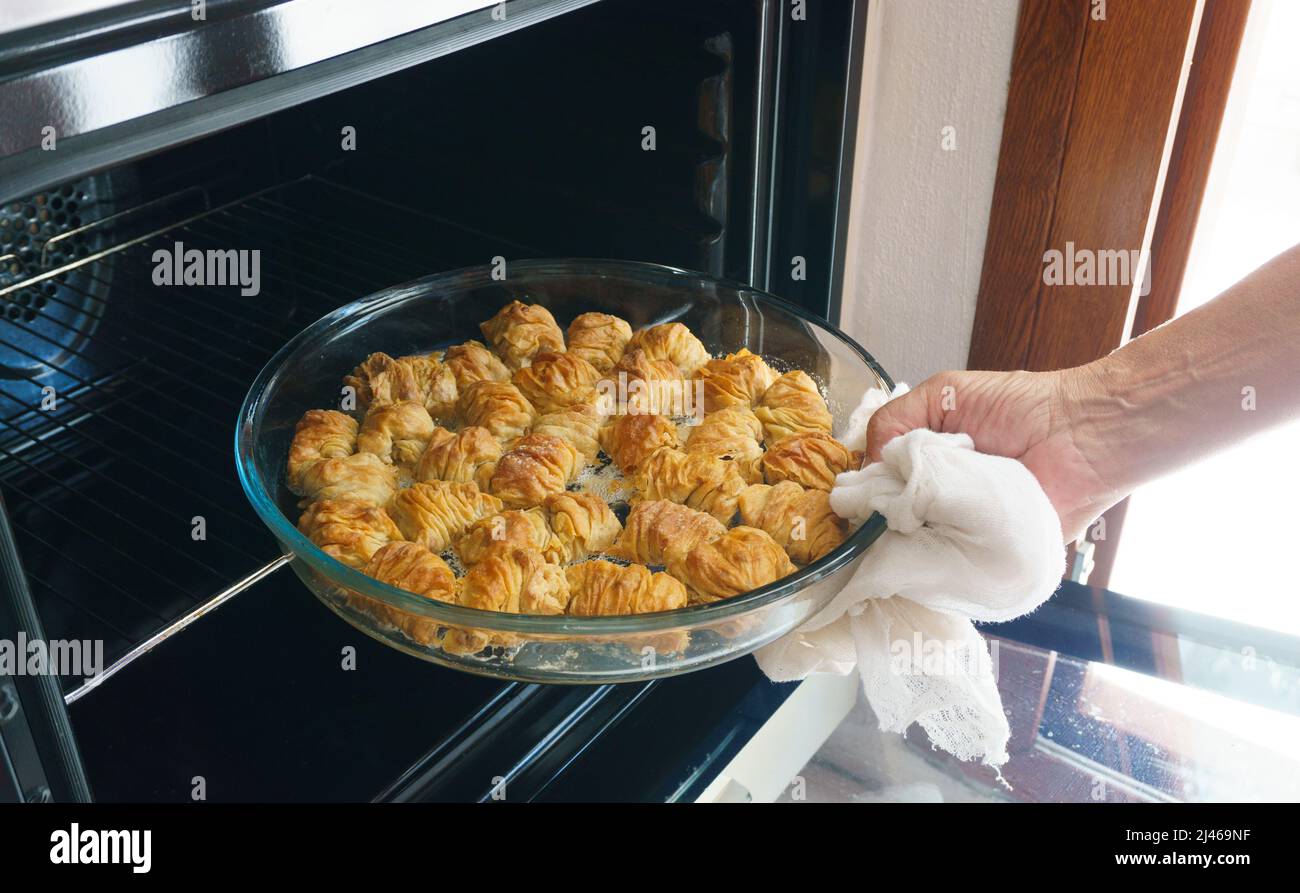 Woman taking a tray of baklava from the oven, homemade Turkish dessert slices with walnut. Ramadan (Ramazan Bayrami) or Sugar (Seker) feast in Turkey. Stock Photo