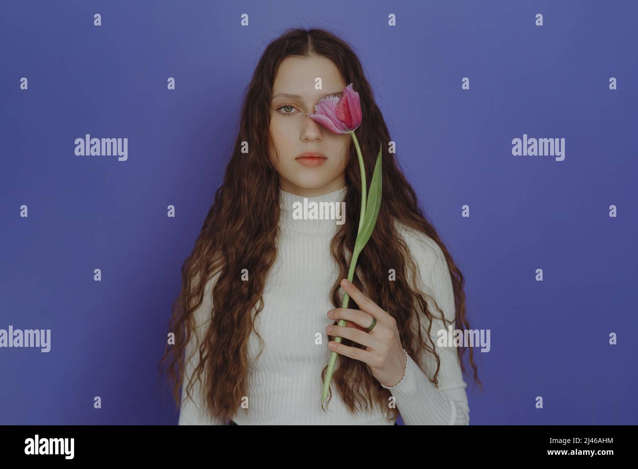 Portrait of a young girl with closed eyes, long hair and a tulip flower. A teenage girl with closed eyes is holding a tulip flower near her face, clos Stock Photo