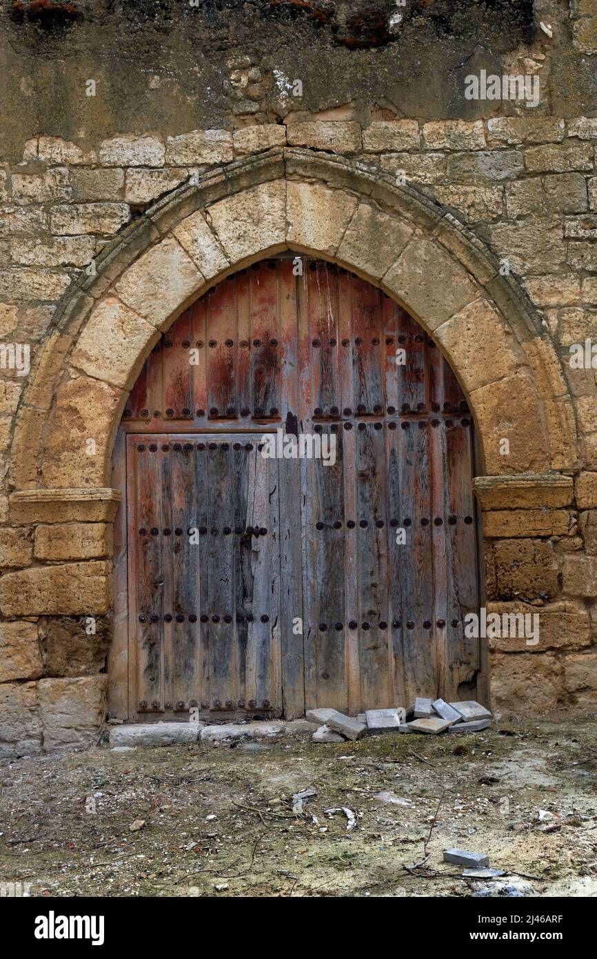 Derelict, arched wooden door on Iglesia de San Miguel, Becerril de Campos, Castile and León, Spain. Stock Photo