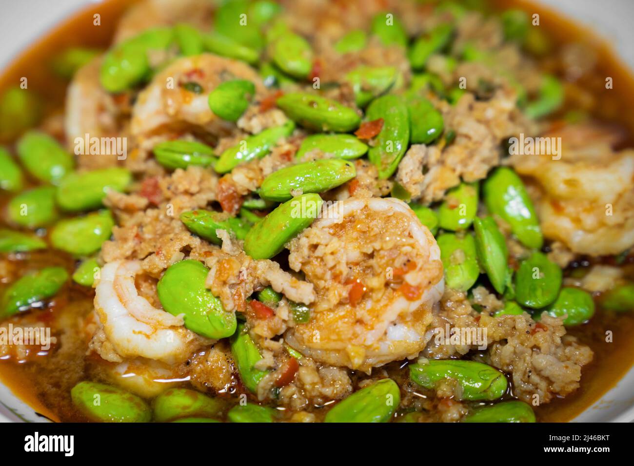 Close up Thai Stir-Fried Stink Beans with Shrimps and spicy shrimp paste sauce in white dish bowl on dark wood table. Stock Photo