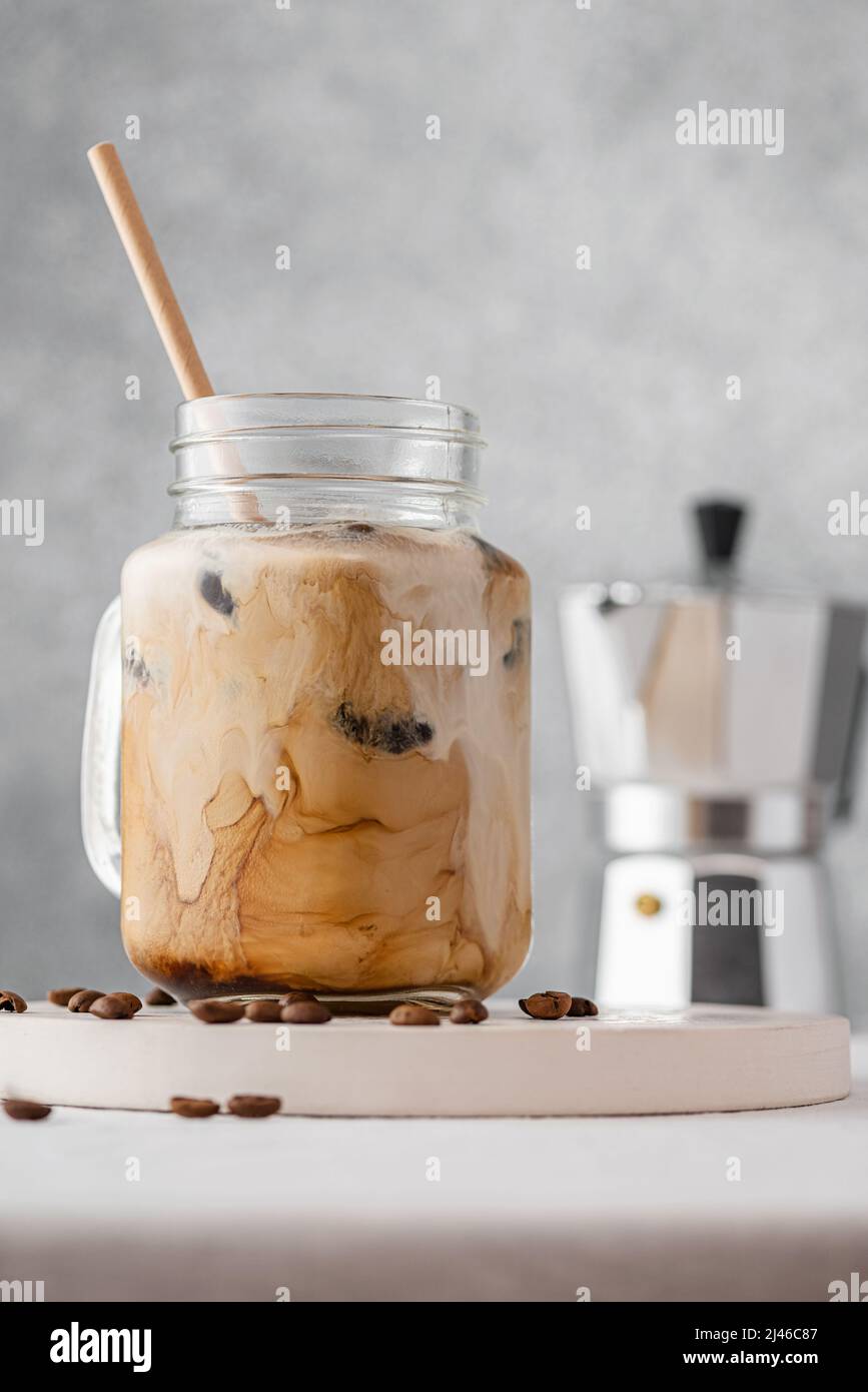 Iced coffee with milk or cream in a glass jar with a straw on gray background. Cold refreshment summer drink. Vertical orientation Stock Photo
