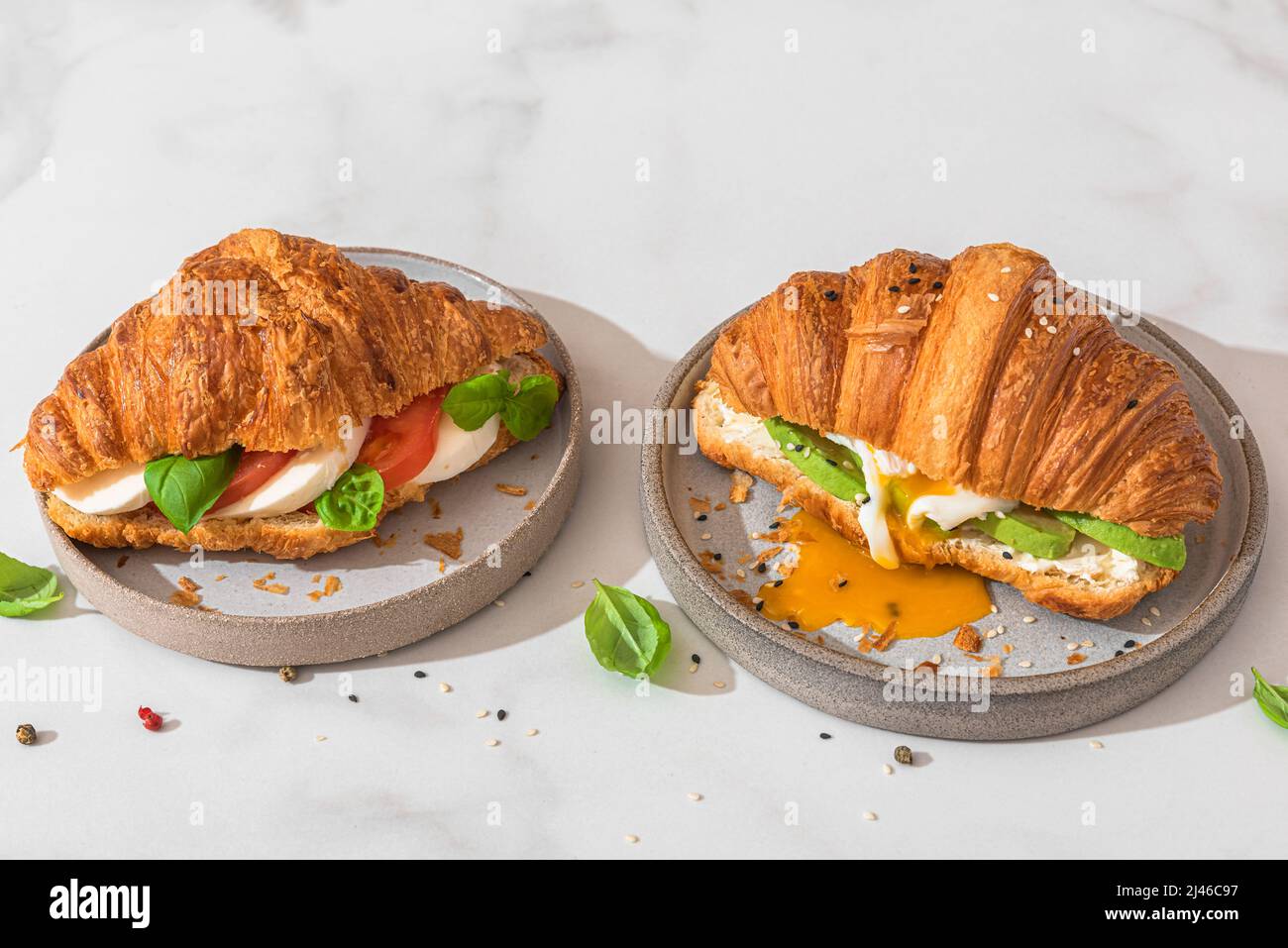 Croissant sandwiches with poached egg, avocado, soft cheese, mozzarella and tomato in a plate on white background. French breakfast. Tasty food Stock Photo