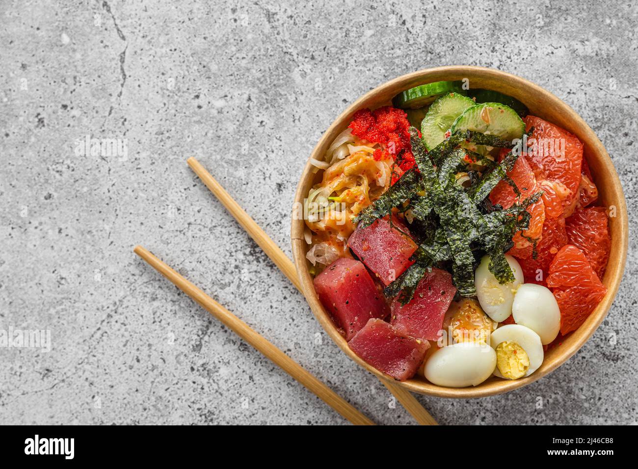 Paper box or package with tuna poke bowl salad for take away or food delivery with chopsticks on gray background. top view. Healthy food Stock Photo