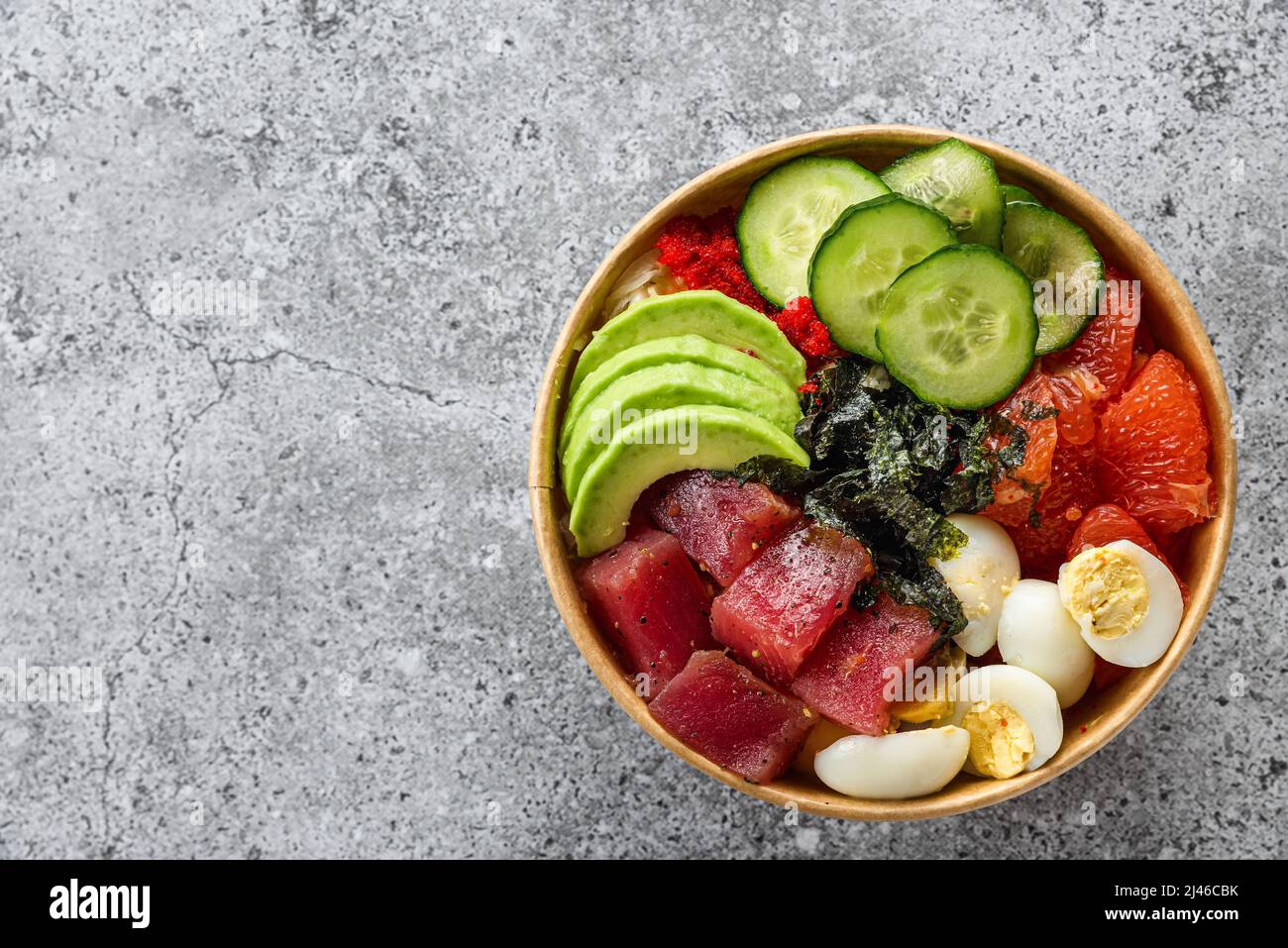 Tuna poke bowl salad with avocado in paper package for take away or food delivery on gray background. Top view with copy space. Healthy food Stock Photo